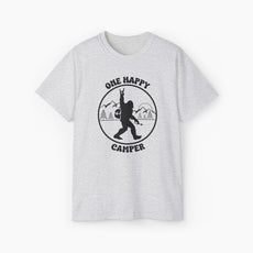 Light grey t-shirt with 'One Happy Camper' text, featuring Bigfoot making a peace sign, set against a subtle background of trees and mountains.
