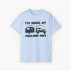 Light blue t-shirt with humorous text 'I'm good at pulling out' featuring an image of a truck pulling a camping van, set against mountains on a plain background.