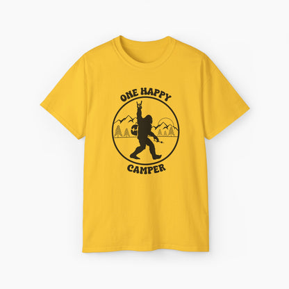 Yellow t-shirt with 'One Happy Camper' text, featuring Bigfoot making a peace sign, set against a subtle background of trees and mountains.