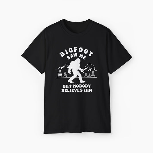 Black t-shirt featuring the humorous text 'Bigfoot saw me, but nobody believes him,' with an image of Bigfoot walking, surrounded by mountains and trees on a plain background.